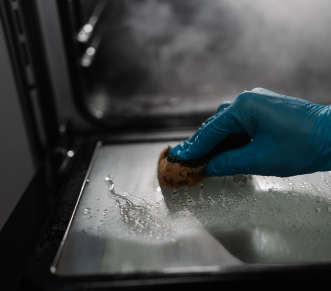 Gloved hand cleaning the interior glass of an oven